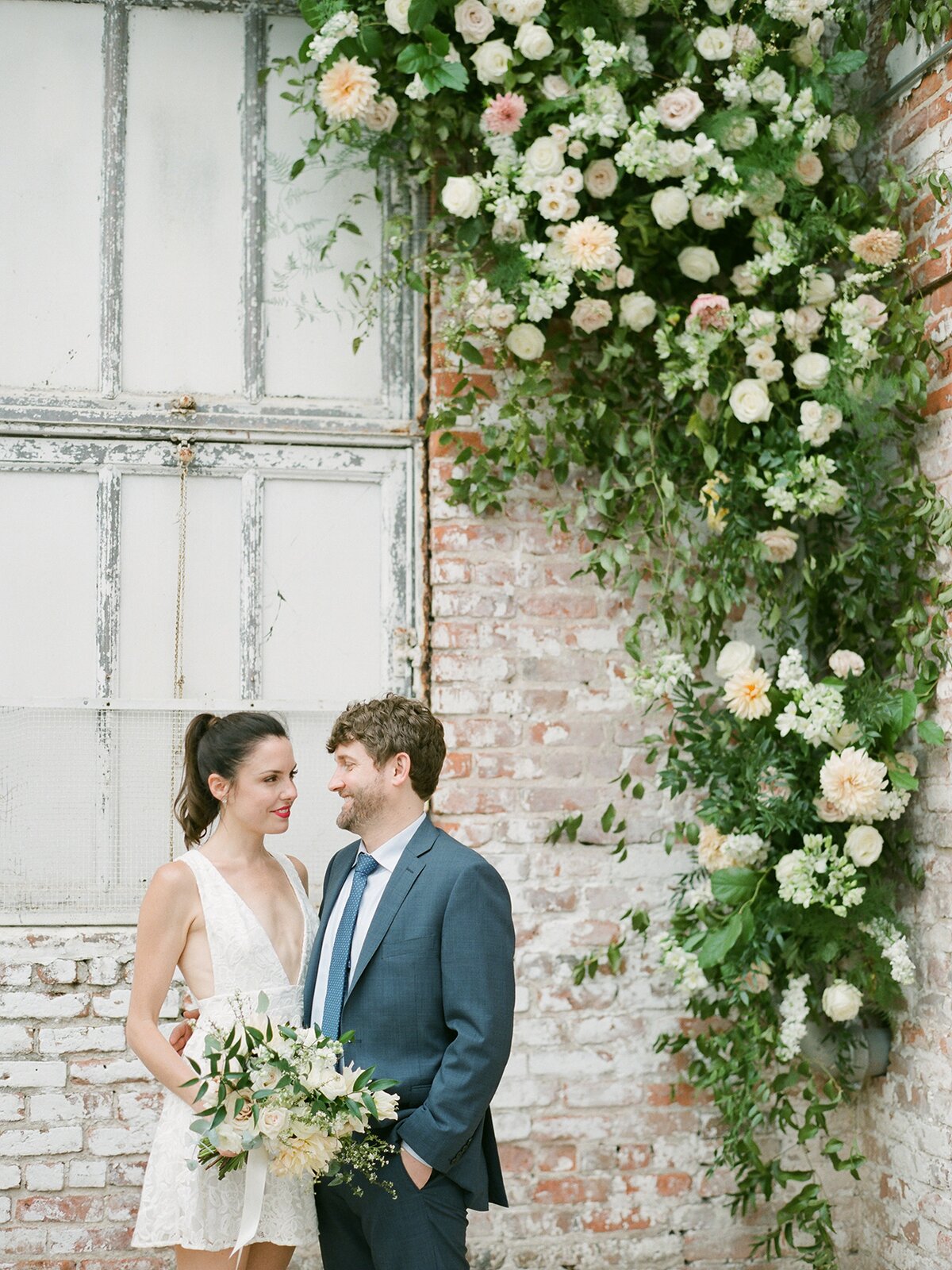 Happy couple standing in front of brick wall with floral garden background