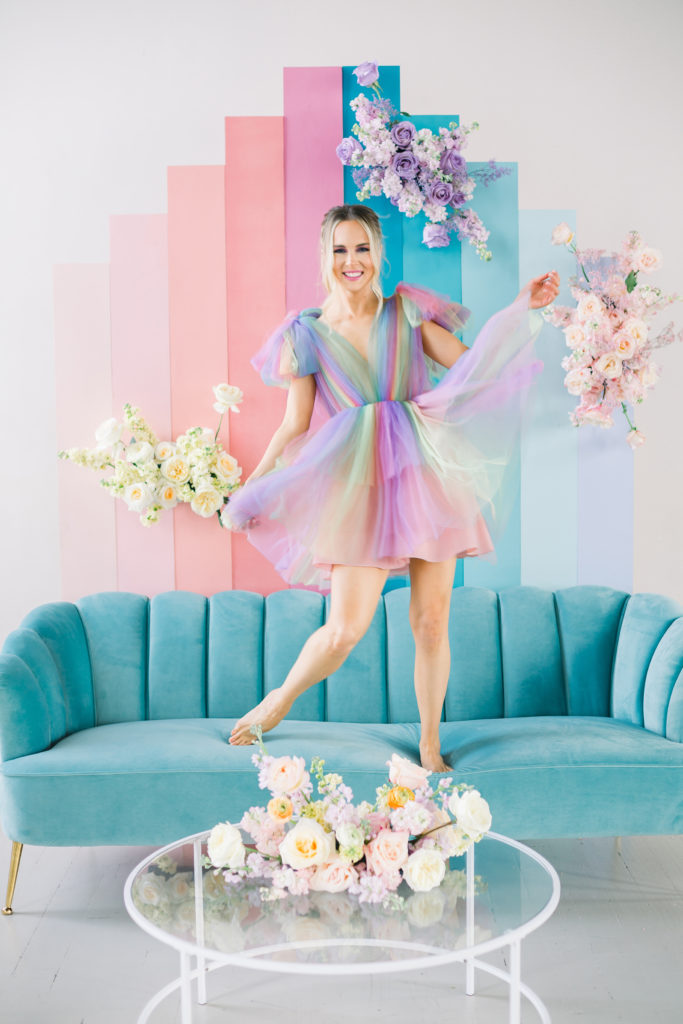 girl standing on pastel blue sofa in a rainbow dress