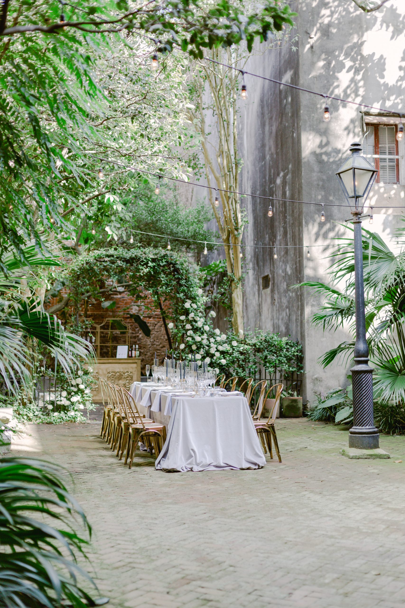 Courtyard seated dinner with gold chairs, black candles and white florals